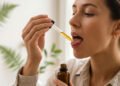 Person placing CBD oil under tongue using a glass dropper for sublingual absorption