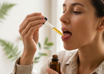 Person placing CBD oil under tongue using a glass dropper for sublingual absorption
