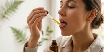Person placing CBD oil under tongue using a glass dropper for sublingual absorption